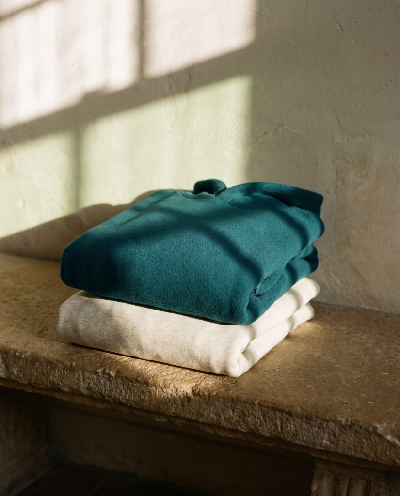 Folded sweatshirts and hoodies on a stone bench in window light